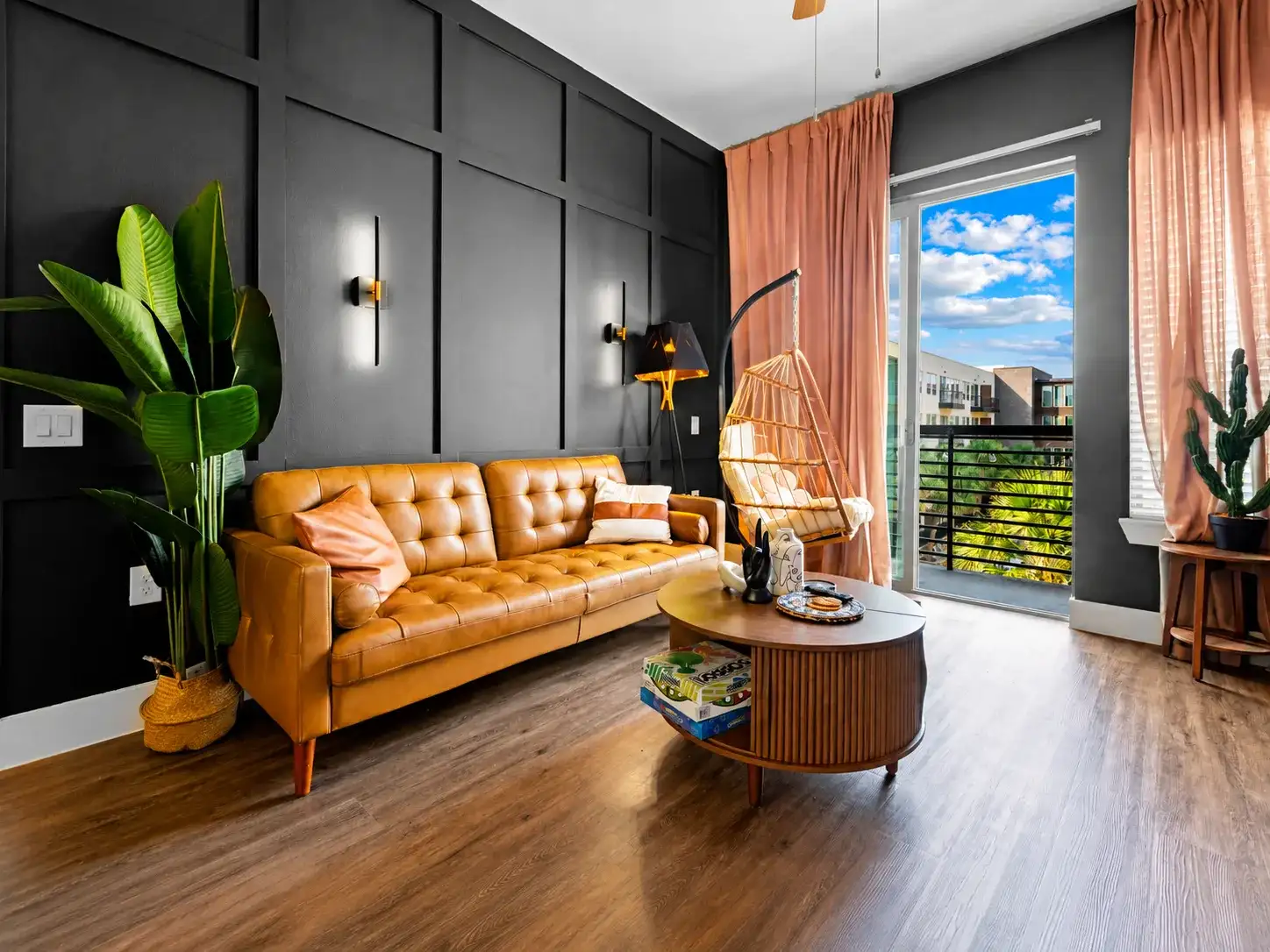 Chic living room with leather sofa, hanging chair, and sunny balcony views