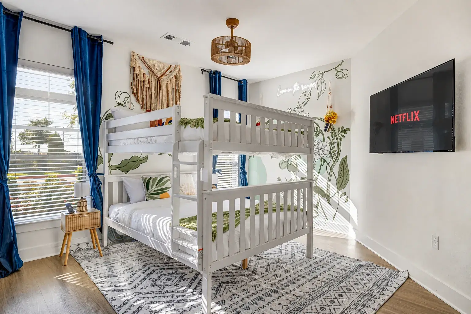Bright bunk room with botanical mural, streaming TV, and sunny windows
