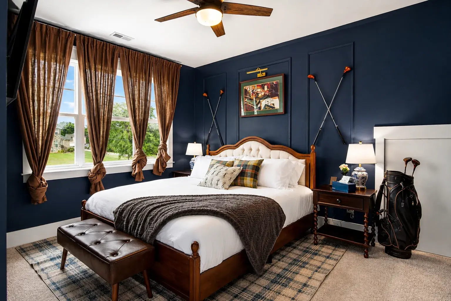 Elegant king bedroom with navy walls, natural light, and golf-inspired decor