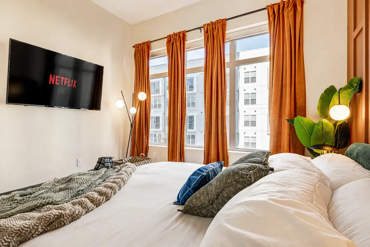 Cozy, light-filled bedroom with plush bedding, large windows, and TV